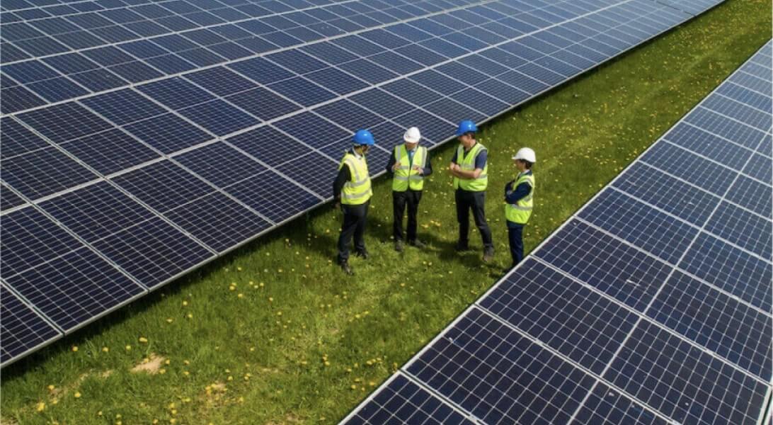 Four technicians positioned between solar panels while discussing