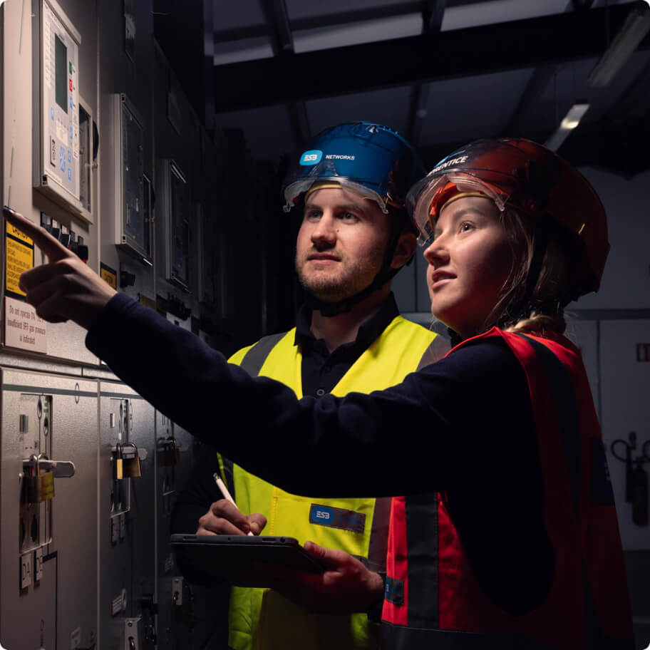Two ESB Networks technicians in safety vests examining a control panel