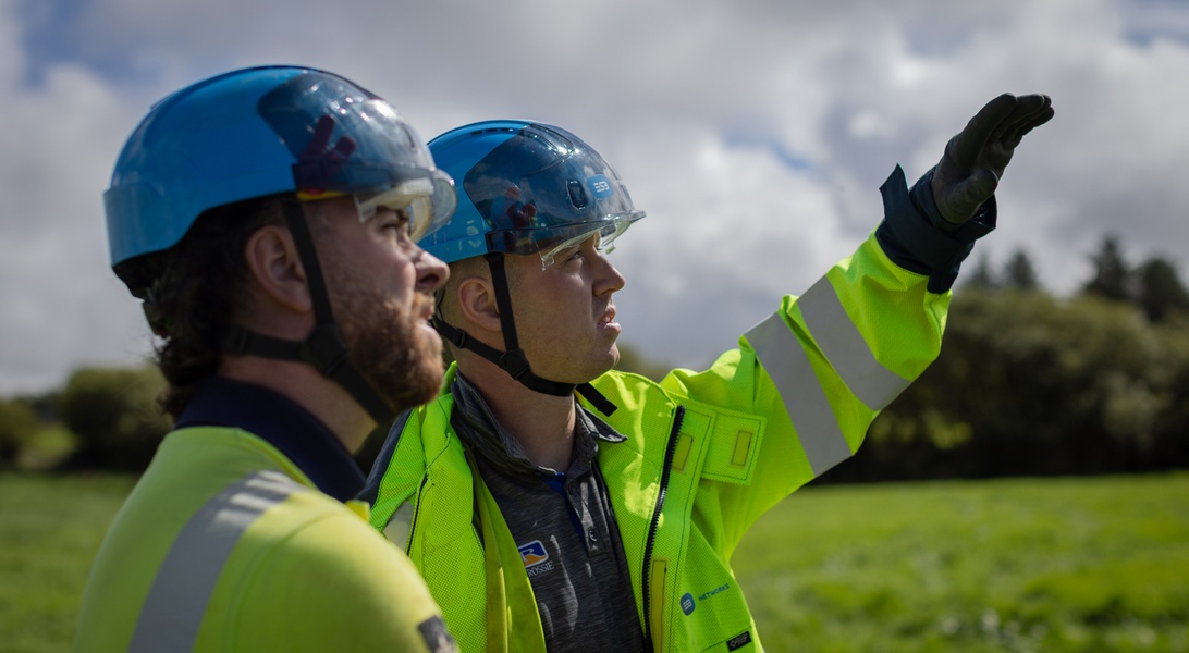 Two ESB Networks field staff in high-visibility safety gear assessing infrastructure in a rural landscape