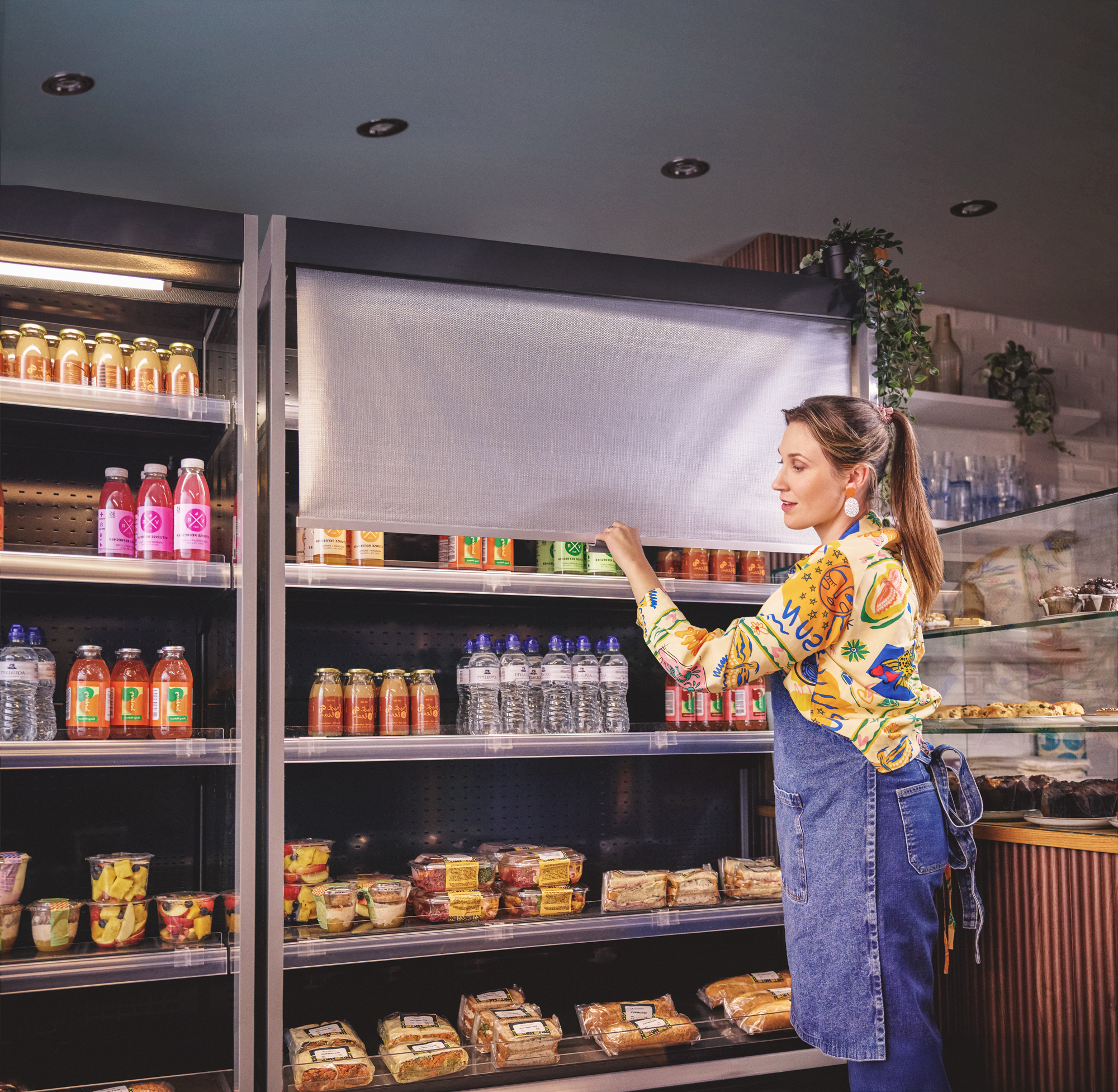 Woman closing blinds of fridge in shop to keep the cool air in for DSF Campaign