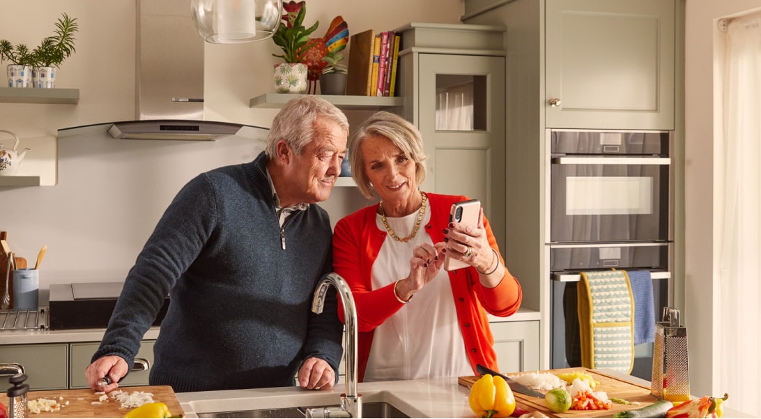 A couple looking at a phone screen in their kitchen.