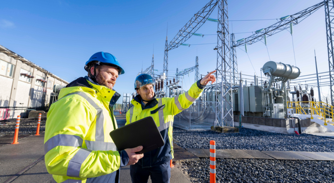 2 men in PPE  standing in front of transformer pointing and looking at it