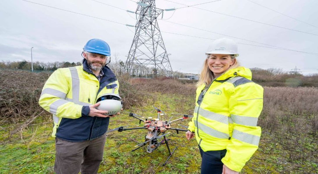 2 workers in PPE beside transmission tower operating a drone