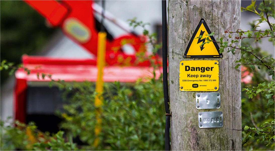 A sign affixed to ESB Networks electric wooden pole line, indicating caution