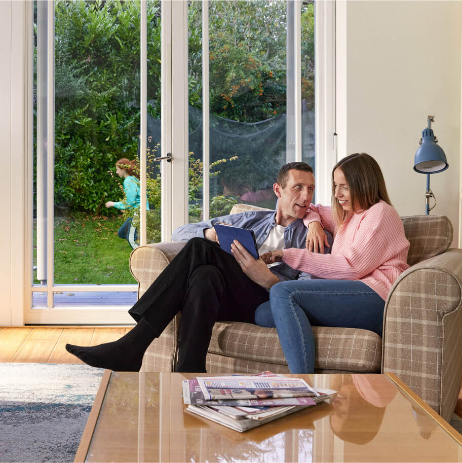 A couple sitting on a couch looking at their tablet