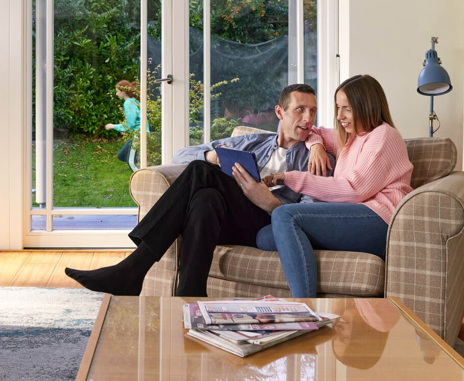 A couple sitting on a couch looking at their tablet