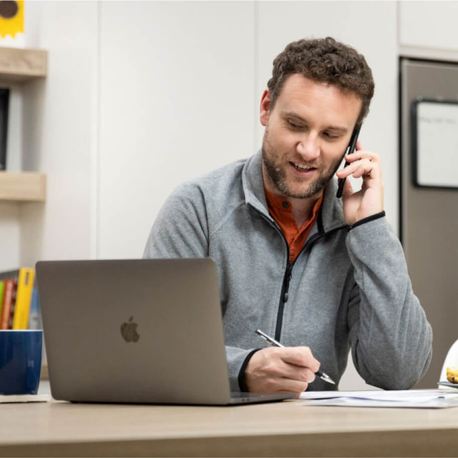 Man smiling on a phone in front of a laptop