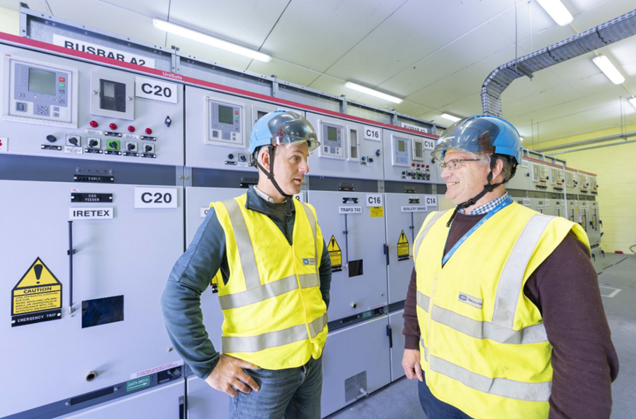 An image of two people standing in front of equipment in a substation