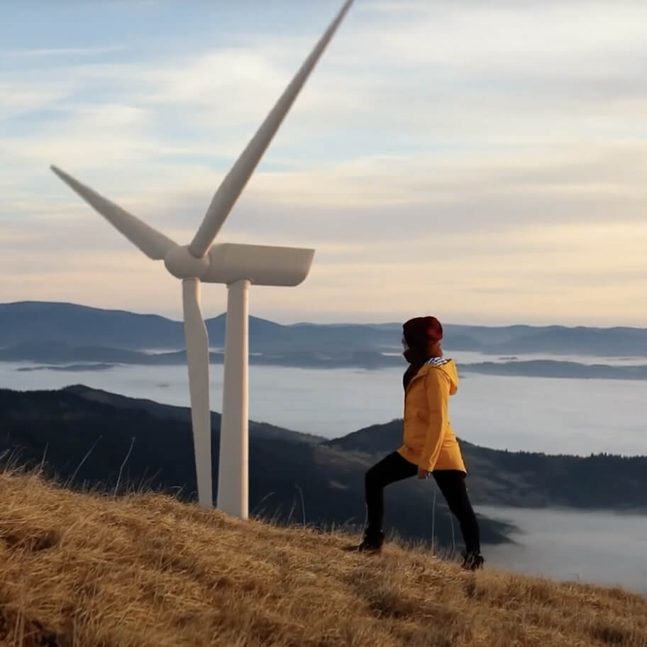 Woman climbing hill with wind turbine and island in the background
